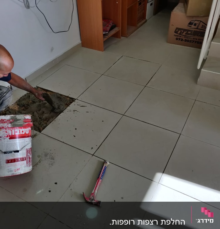 אדם מתקין אריחי רצפה עם מלט ודלי